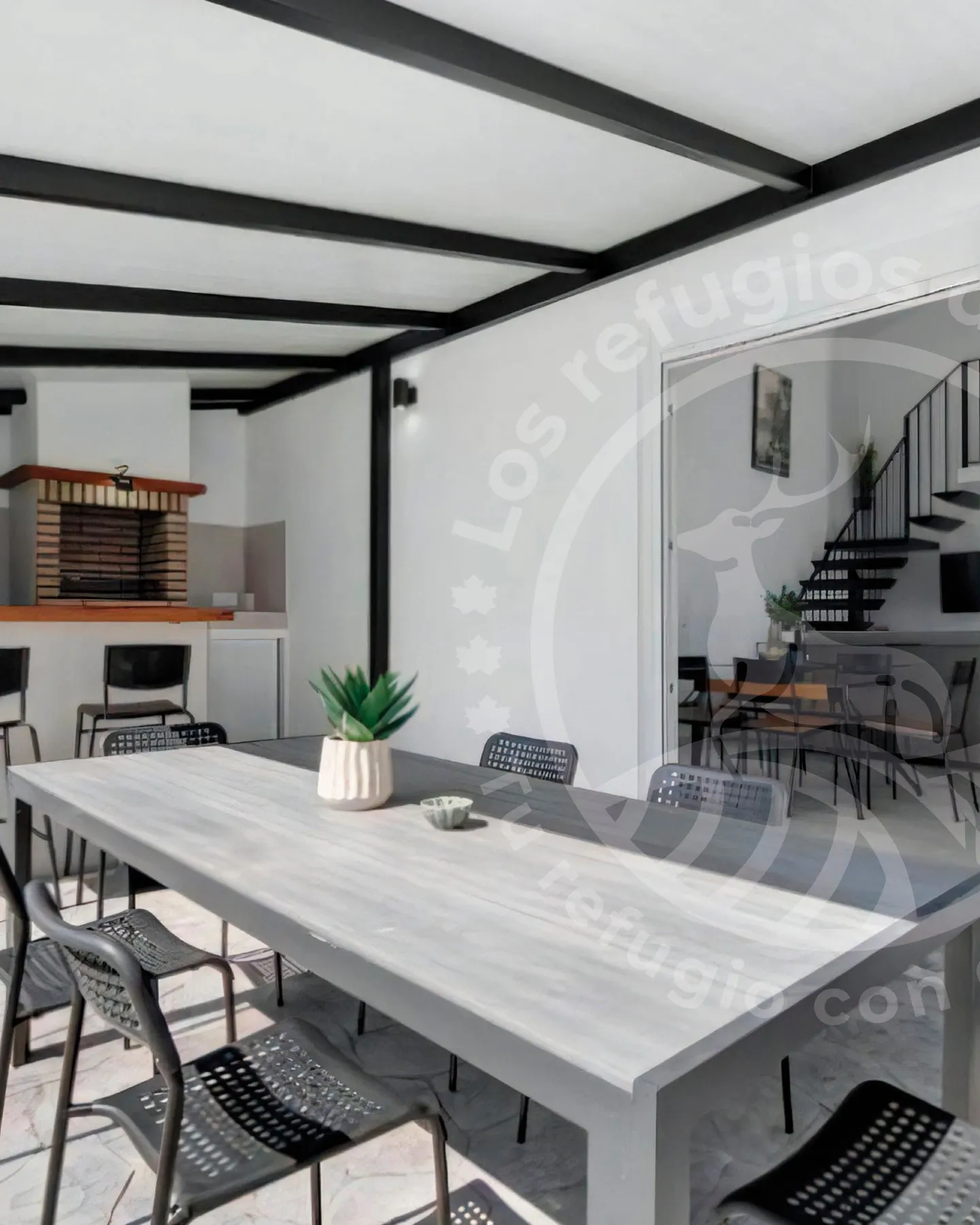 Long table with chairs under the covered porch, with the barbecue behind and the living room in view